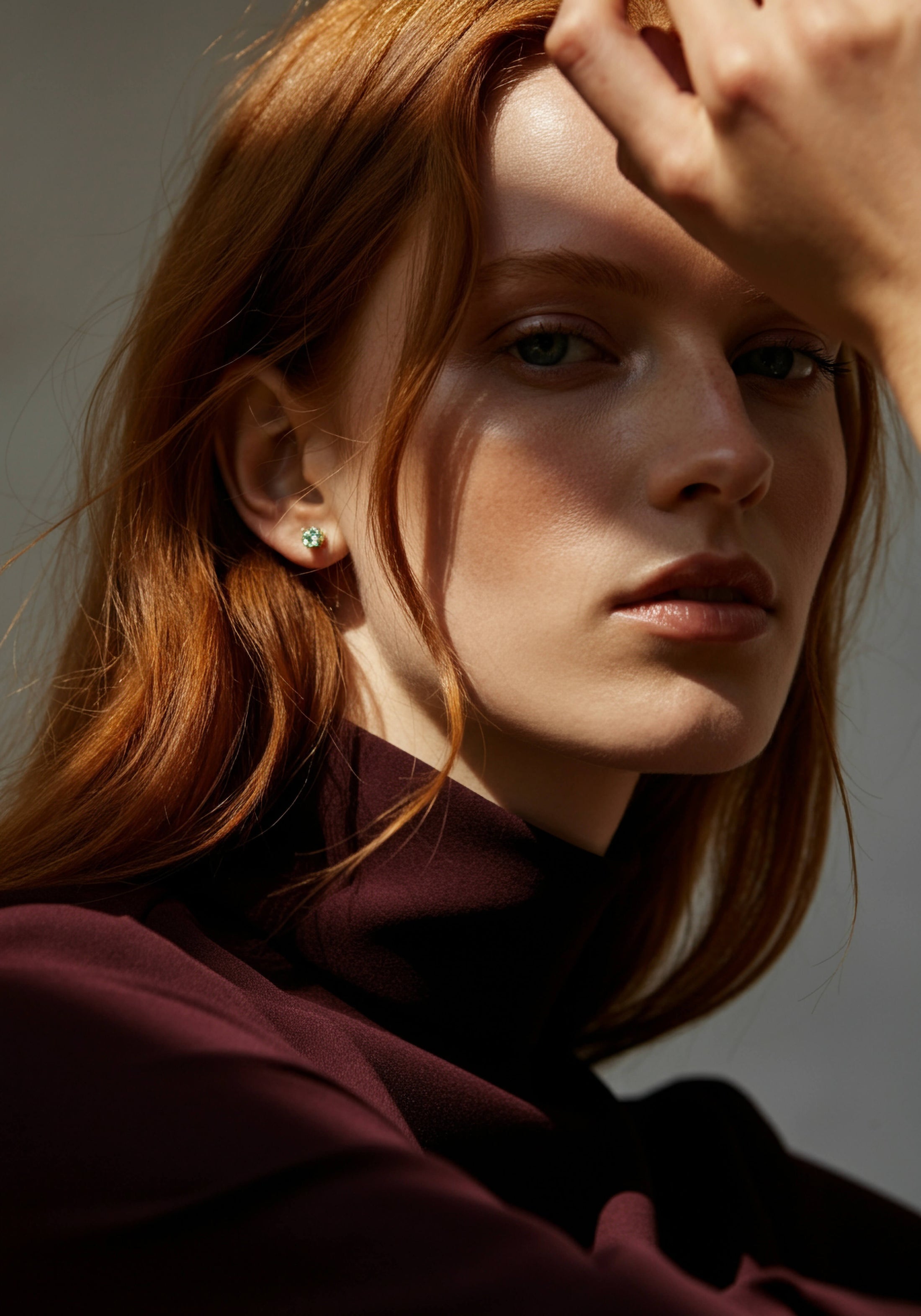 Model with red hair and simple diamond stud looks at camera.